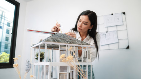 Professional young beautiful architect engineer using ruler and pencil measuring model roof length at modern office with blueprint pinned behind. Creative design and living concept. Immaculate.の写真素材