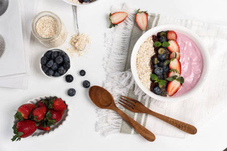 Presented by fruits putting yogurt toppings with strawberry, berry, oats and chia seed decorated by peppermint in white bowl. Pink background. Set of healthy dairy product choice.の写真素材
