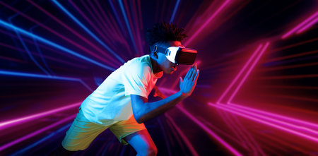 African man wearing VR headset while exercising at an abstract background with glowing pink and blue color. Attractive male model playing fitness while wearing white shirt. Technology. Ingenuity.の写真素材