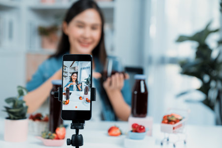 Selective focus smartphone with smiling young beautiful Asian reviewing mixed strawberry and cherry juice detox drink, presenting healthy product promotion selling on social media online. Stratagem.の写真素材