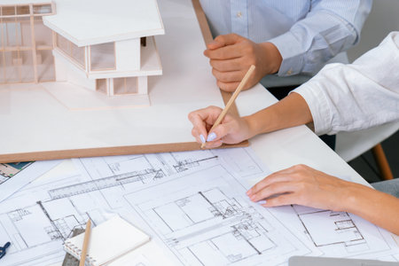 Top view image of professional beautiful young architect hand drafts blueprint while asian...