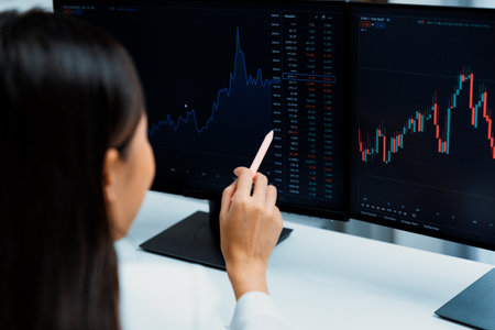 Young beautiful Asian businesswoman pointing with pen in exchange stock market on pc screen at back side view, analyzing profit at modern office, investing high profit valed in wealth. Stratagem.の写真素材