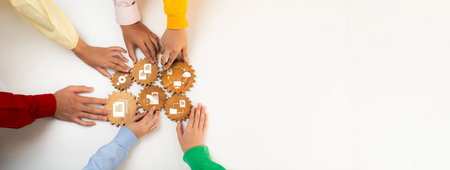 A group of diverse hands collaborates to arrange gear icons on a neutral background, symbolizing teamwork and innovative management strategies for business success.の写真素材