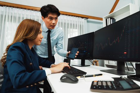 Smiling Asian businessman showing dynamic stock market data on phone to woman partner searching on...