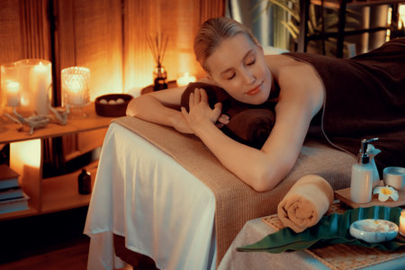 Caucasian woman customer enjoying relaxing anti-stress spa massage and pampering with beauty skin recreation leisure in warm candle lighting ambient salon spa at luxury resort or hotel. Quiescentの写真素材