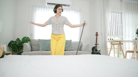 Smiling housekeeper with headphone listen music while cleaning floor. Happy smart caucasian mother mopping floor while dancing and singing to lively song at living room. Mom doing housework. Pedagogyの写真素材