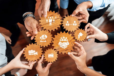 A group of diverse individuals gathers to hold wooden gears featuring business icons, symbolizing...
