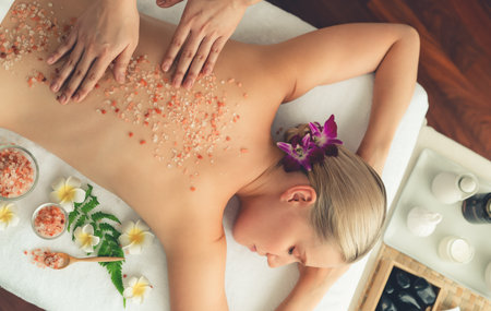 Panorama top view woman customer having exfoliation treatment in luxury spa salon with warmth candle light ambient. Salt scrub beauty treatment in health spa body scrub. Quiescentの写真素材