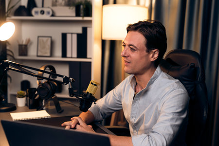Host channel smart broadcaster talking on live social media application searching on laptop, broadcasting streamer wearing headphone using mic at modern home office studio in warm lighting. Pecuniary.の写真素材