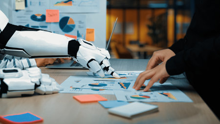 In a modern office scene, a robot hand collaborates with a human hand on data analysis. Business...