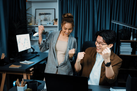 Successful wealthy of smiling business trader with partner in casual suit earning high profit raising fist up in exchange stock market investment in technology at modern office at night. Infobahn.の写真素材