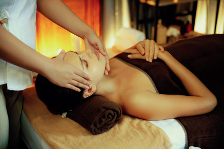 Caucasian woman enjoying relaxing anti-stress head massage and pampering facial beauty skin recreation leisure in warm candle lighting ambient salon spa in luxury resort or hotel. Quiescentの写真素材