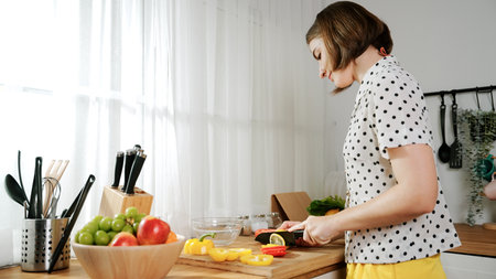 Energetic mother making salad for breakfast at modern kitchen while chopping vegetable surrounded with kitchenware. Smart female house keeper cooking and preparing food. Healthy lifestyle. Pedagogy.の写真素材