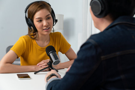 Smiling radio influencer host wearing headphone interviewing woman speaker sharing information to listeners on social media online website live streaming channel at morning at studio record. Infobahn.の写真素材