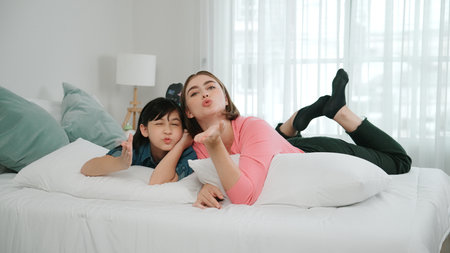 Happy asian daughter and smart mom lie on bed while looking at camera. Energetic family spend time...
