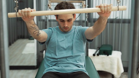 Man performing seated core exercise on pilates trapeze holding bar to strengthen arms and core...