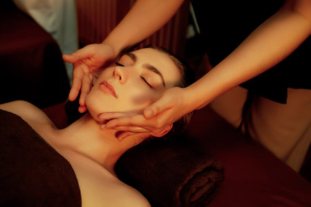 Caucasian woman enjoying relaxing anti-stress head massage and pampering facial beauty skin recreation leisure in warm candle lighting ambient salon spa in luxury resort or hotel. Quiescentの写真素材