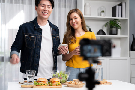 Chef influencers reading comment on phone for answer time on social media cooking show channel live streaming menu dish mix salad, bun bread wholegrain and hamburger record by video camera. Infobahn.の写真素材
