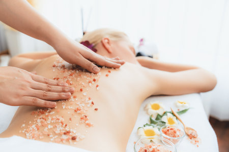 Closeup woman customer having exfoliation treatment in luxury spa salon with warmth candle light ambient. Salt scrub beauty treatment in health spa body scrub. Quiescentの写真素材