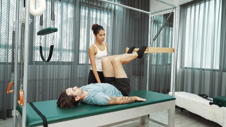 Skilled pilates instructor assisting a client in leg lift exercise on Cadillac equipment. Female...