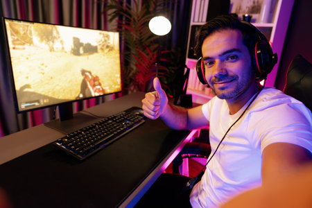 Smart gaming streamer looking at camera making self photo shooting with showing against with battle game on pc screen, using headset and mic talking others at digital neon light studio room. Surmise.の写真素材
