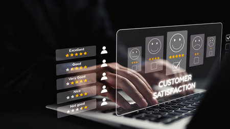 A person interacts with a laptop, analyzing customer satisfaction through smiley face icons and star ratings, highlighting the importance of feedback for business success.の写真素材