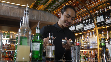 Asian bartender pouring mixed cocktail juice liqueur all ingredient into sliver shaker alcohol...
