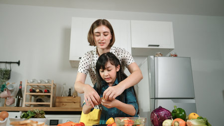 Smart caucasian mother and asian girl cooking together and chopping vegetable or preparing salad for dinner. Happy mom and daughter making healthy food with fresh food. Healthy food concept. Pedagogy.の写真素材