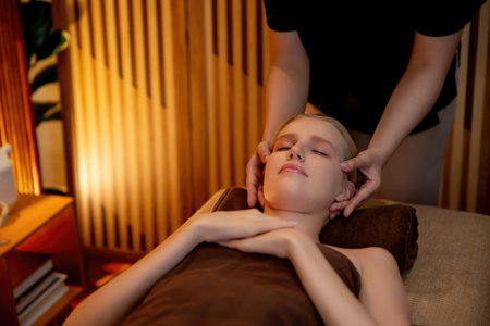 Caucasian woman enjoying relaxing anti-stress head massage and pampering facial beauty skin recreation leisure in warm candle lighting ambient salon spa in luxury resort or hotel. Quiescentの写真素材
