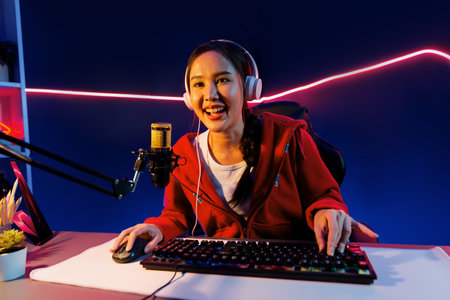 Host channel of smiling beautiful Asian girl streamer playing online game wearing headphone talking with viewers media online recording phone. Esport skilled team players in neon blue room. Stratagem.の写真素材