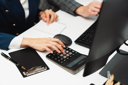 Cropped hands businessman with coworker calculating with calculator manuals financial and accounting...