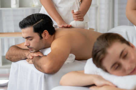 Hot herbal ball spa massage body treatment, masseur gently compresses herb bag on couple customer body. Tranquil and serenity of aromatherapy recreation in day lighting ambient at spa salon. Quiescentの写真素材