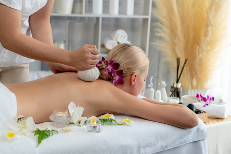 Hot herbal ball spa massage body treatment, masseur gently compresses herb bag on woman body. Tranquil and serenity of aromatherapy recreation in day lighting ambient at spa salon. Quiescentの写真素材