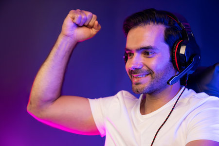 Close up winner smart streamer playing online game wearing headphones raising fist up on streaming gamer with social media. Esport skill team player online digital at neon light studio room. Surmise.の写真素材
