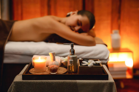 Aromatherapy massage ambiance or spa salon composition setup with focus decor candles and spa accessories on blurred woman enjoying blissful aroma spa massage in resort or hotel background. Quiescentの写真素材