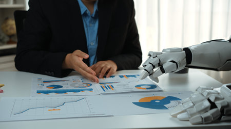 A professional setting showcasing a business meeting where a human and a robot collaborate over charts and graphs, focusing on data-driven strategy and analysis.Noogenesisの写真素材