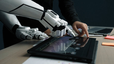A human hand interacts with a robotic hand on a digital tablet, showcasing a collaboration between...