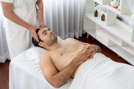 Caucasian man enjoying relaxing anti-stress head massage and pampering facial beauty skin recreation leisure in dayspa modern light ambient at luxury resort or hotel spa salon. Quiescentの写真素材