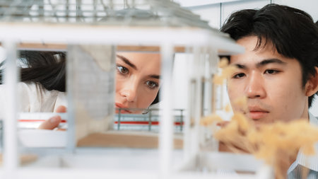 Close up of cooperative professional engineer working together to measuring house model structure. Young beautiful architect measure house model while male engineer support performance. Immaculate.の写真素材