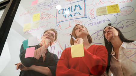 Creative business team brainstorming and sharing marketing idea about start up project by writing down on colorful sticky note at glass board modern meeting room. Working together. Immaculate.の写真素材