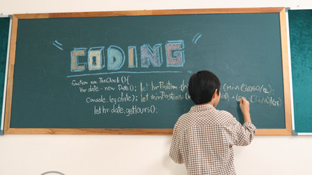 Energetic elementary student standing at blackboard while writing coding engineering prompt and...