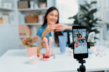 Selective focus phone with young beautiful Asian showing cosmetic makeup lipstick matte pastel color testing bestseller collection on arm test promotion on social media online recording. Stratagem.の写真素材