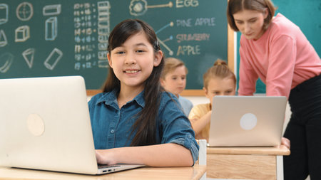 Asian girl looking at camera while coding. Multicultural student learning about AI while teacher...