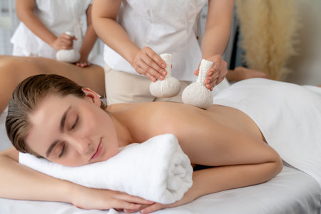 Hot herbal ball spa massage body treatment, masseur gently compresses herb bag on couple customer body. Tranquil and serenity of aromatherapy recreation in day lighting ambient at spa salon. Quiescentの写真素材