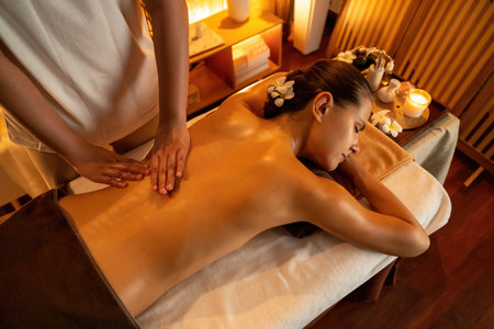 Caucasian woman customer enjoying relaxing anti-stress spa massage and pampering with beauty skin recreation leisure in warm candle lighting ambient salon spa at luxury resort or hotel. Quiescentの写真素材
