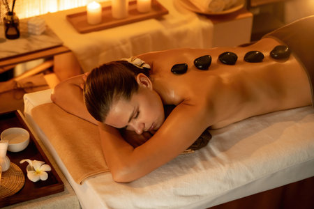 Hot stone massage at spa salon in luxury resort with warm candle light, blissful woman customer enjoying spa basalt stone massage glide over body with soothing warmth. Quiescentの写真素材