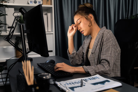 Businesswoman working on computer with stretching arm up and down manner with body health ache of strain overwork unfinished project job on website at late over night time at modern office. Infobahn.の写真素材