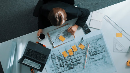 Top down view civil engineer writing sticky note and looking at laptop. Aerial view architect sitting at meeting table while using computer analysis and calculate building structure.の写真素材