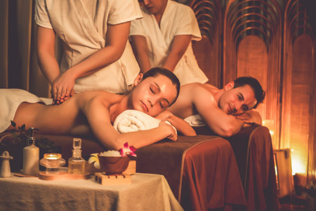 Caucasian couple customer enjoying relaxing anti-stress spa massage and pampering with beauty skin recreation leisure in warm candle lighting ambient salon spa at luxury resort or hotel. Quiescentの写真素材