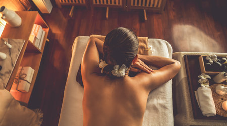 Top view woman customer enjoying relaxing anti-stress spa massage and pampering with beauty skin recreation leisure in warm candle lighting ambient salon spa at luxury resort or hotel. Quiescentの写真素材